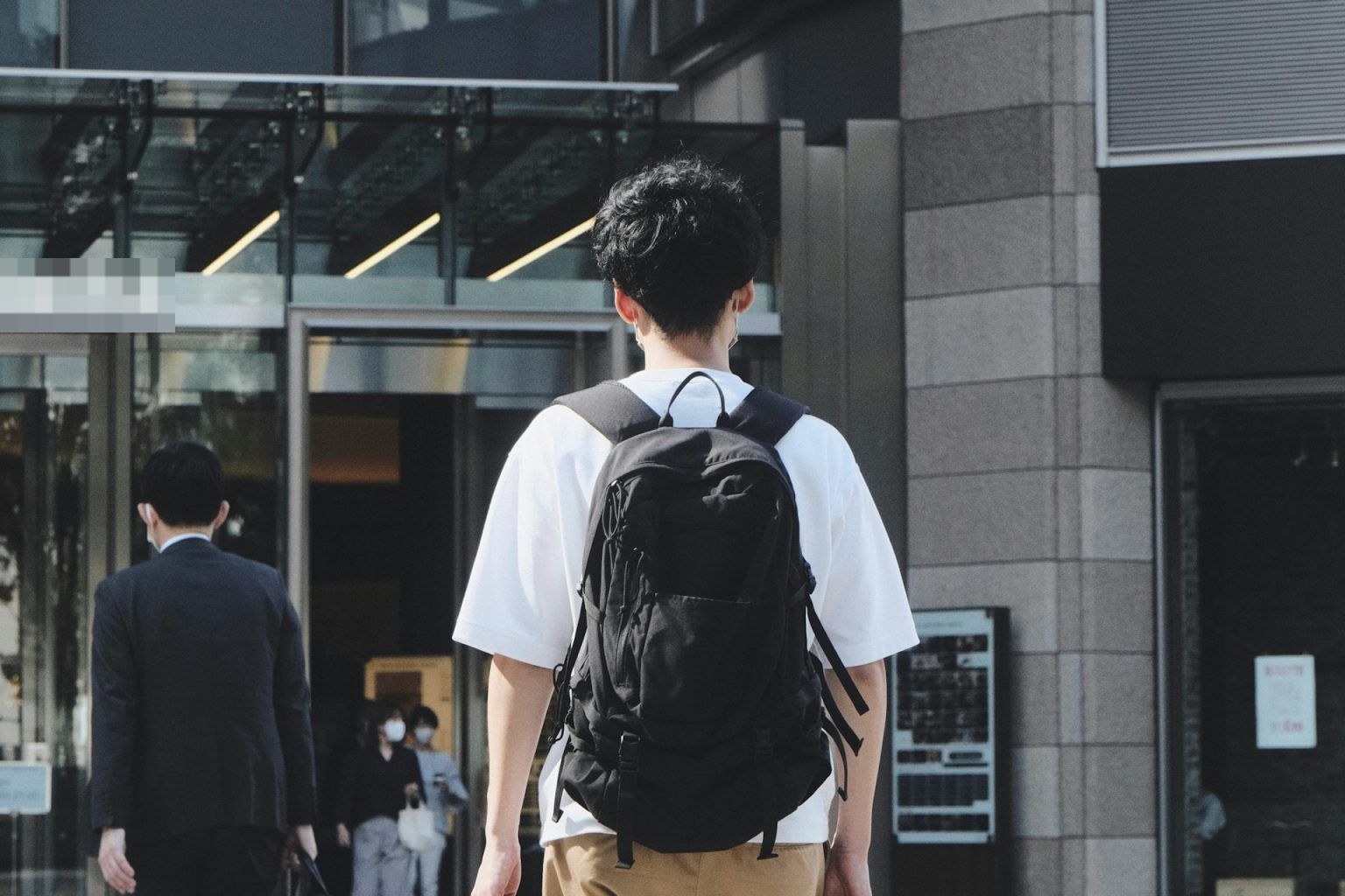 オフィスビルの入口へ向かって歩く、リュックを背負った若い社員