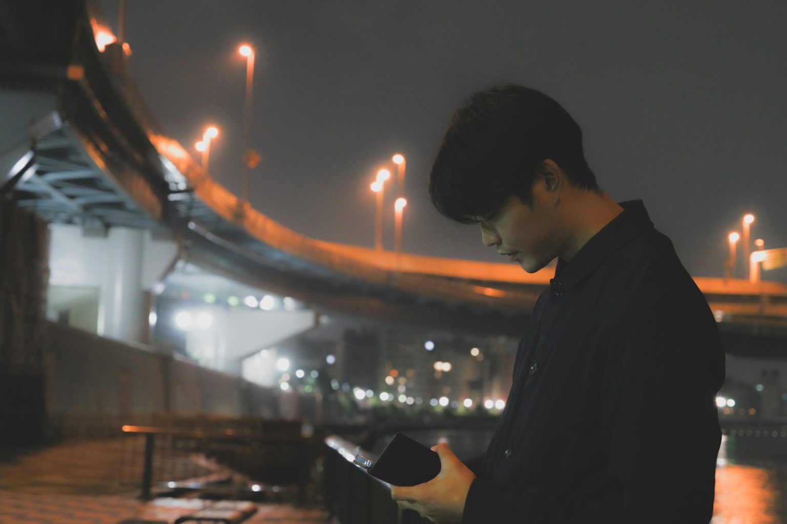 夜の川沿いで手元の端末を見つめる若いエンジニア