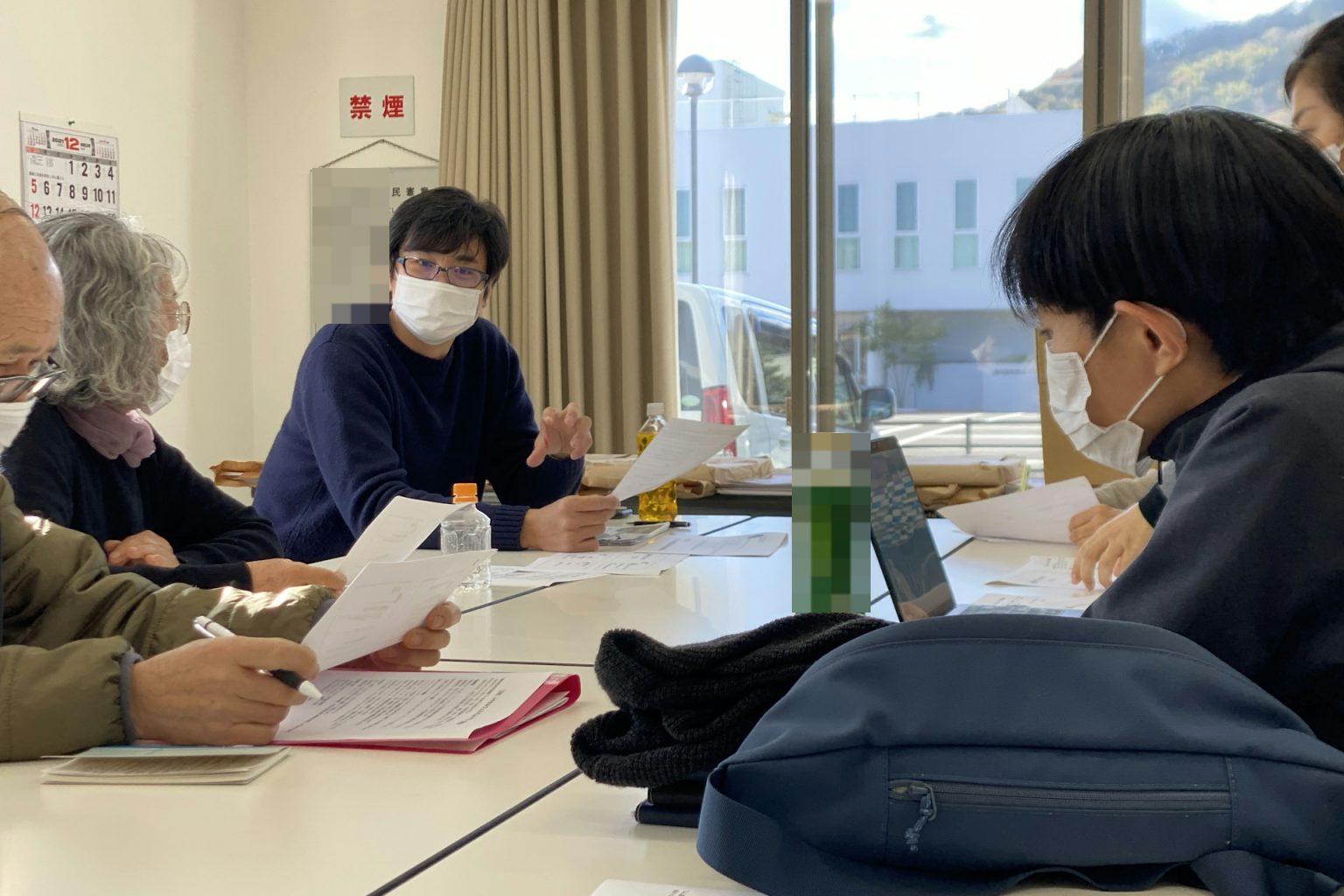 会議室のテーブルを囲んで資料を見ながら話し合う人たち