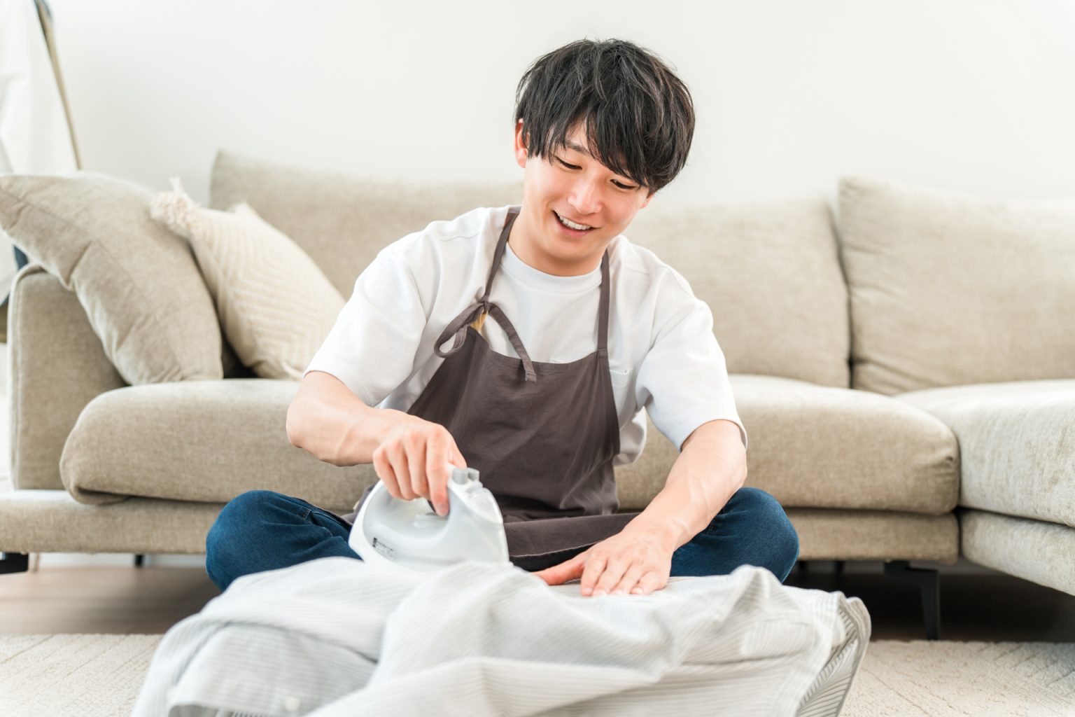 ソファの前で洗濯物を整えるエプロン姿のスタッフ