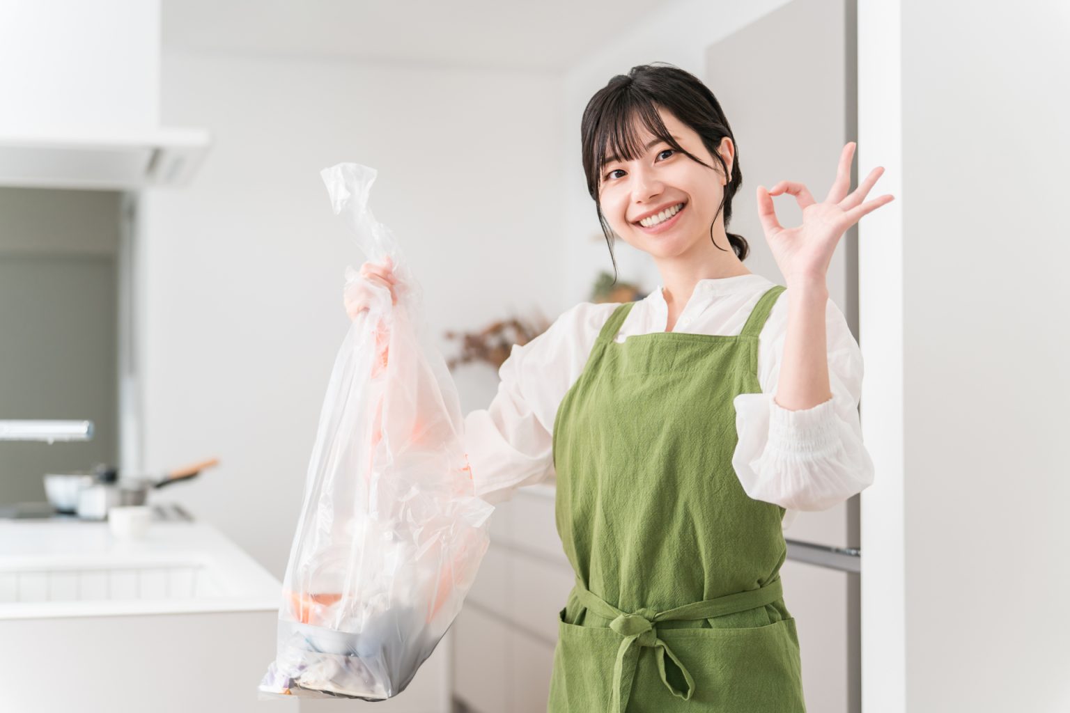 キッチンでごみをまとめながら笑うエプロン姿のスタッフ