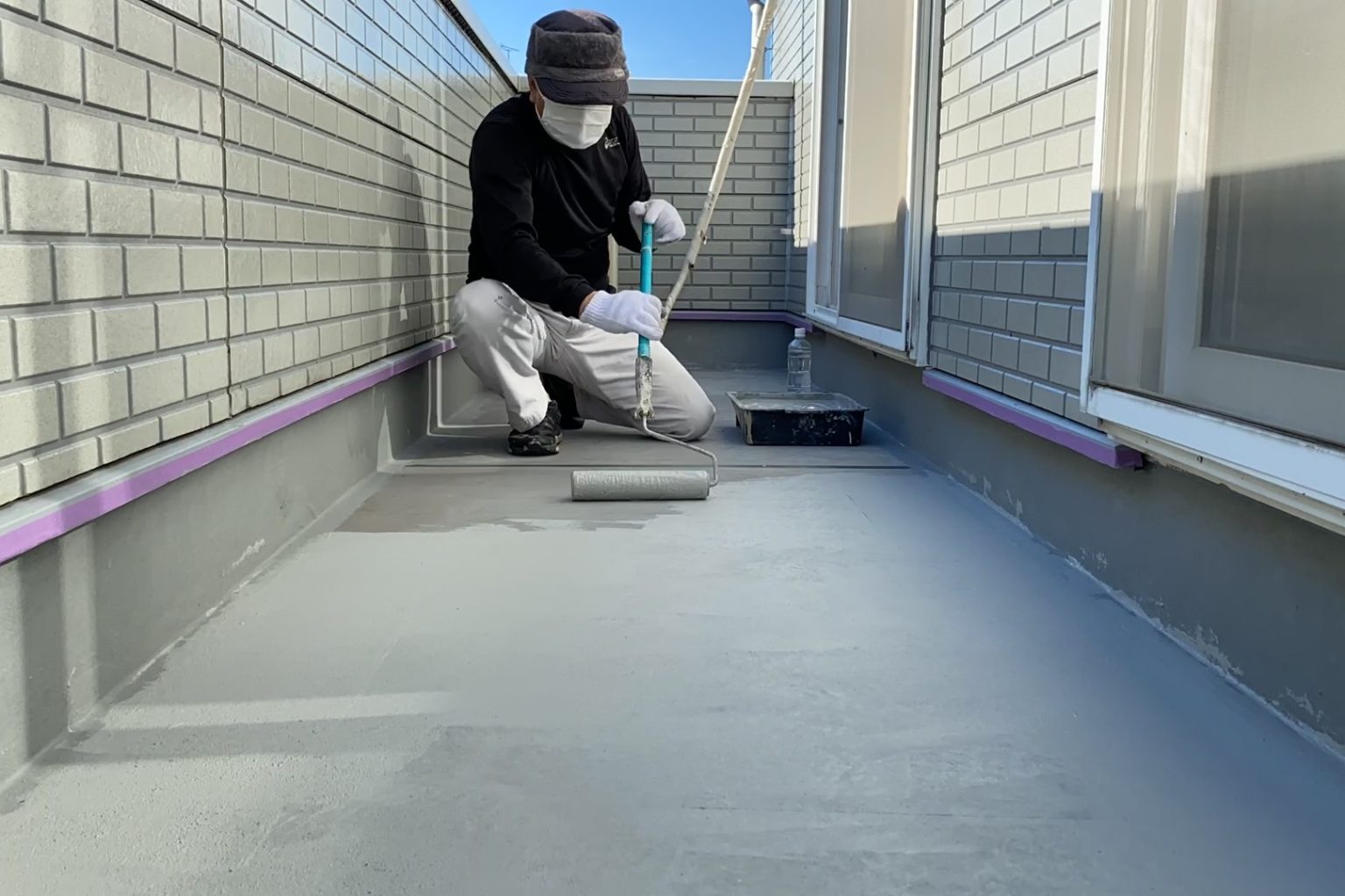 バルコニーの床にローラーで防水塗料を塗っている職人