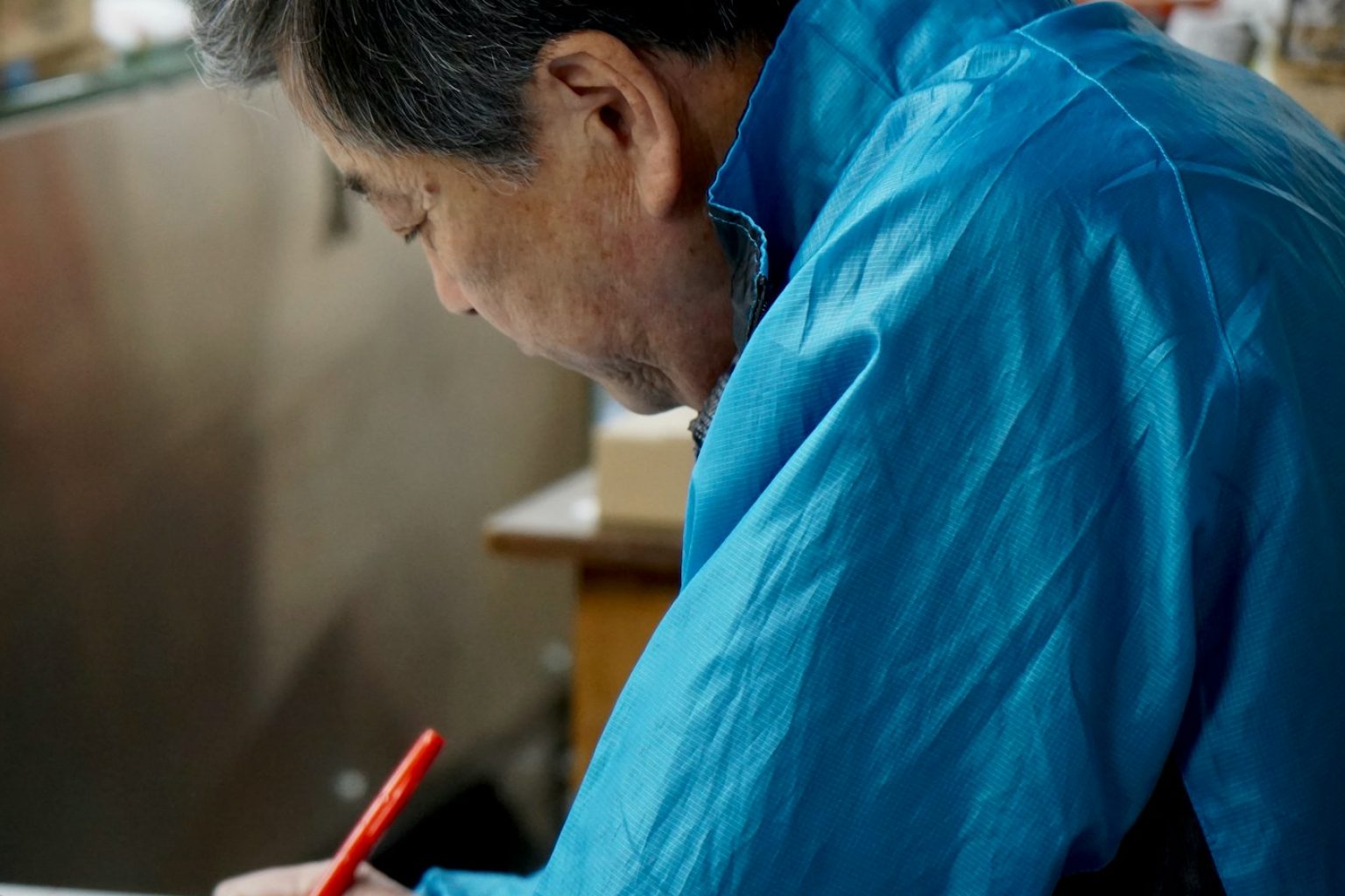 赤いペンで伝票に書き込む、青い上着の年配の社員
