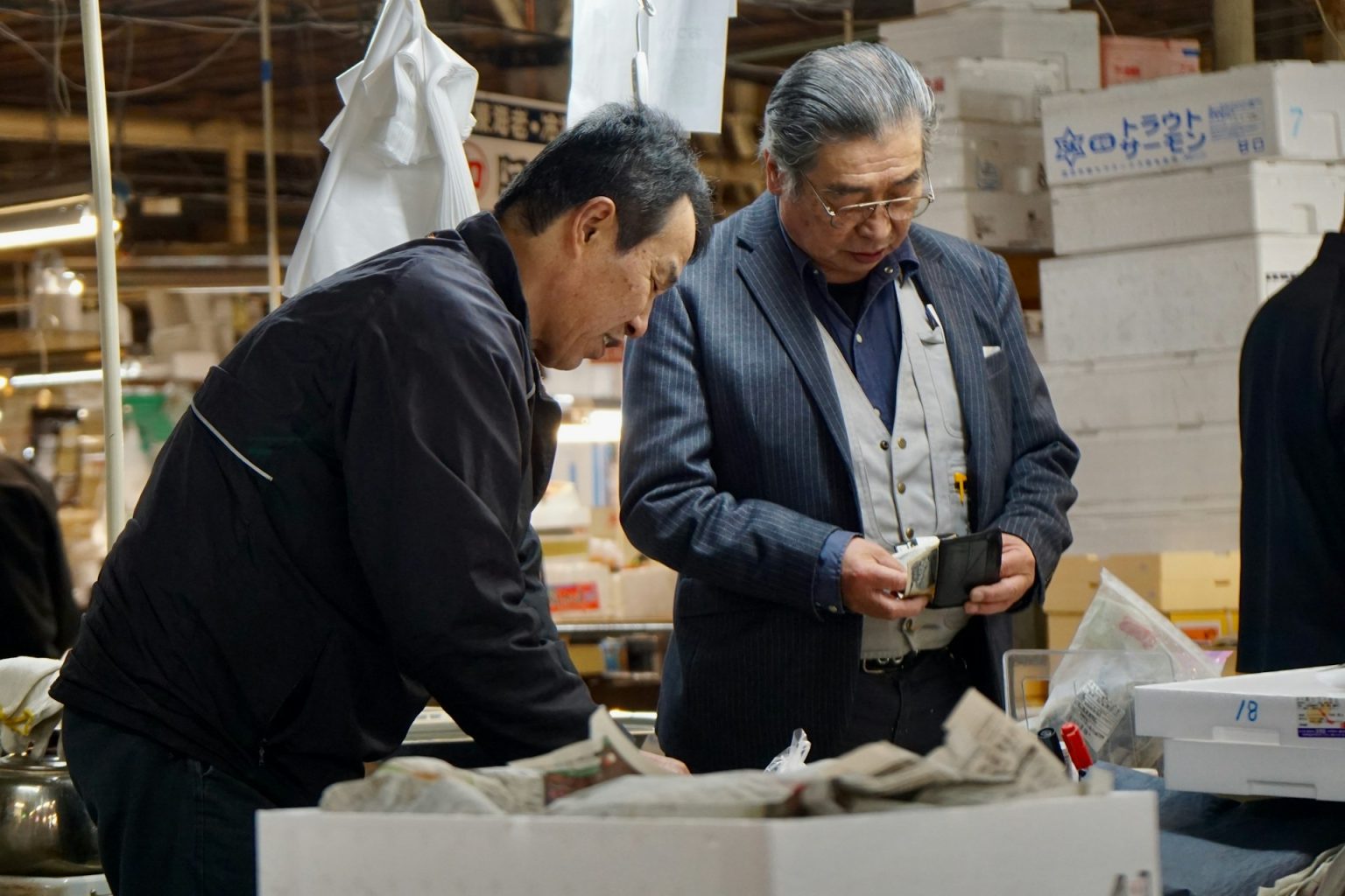 市場の売り場で、発泡スチロールの箱を前に取引をする二人の男性