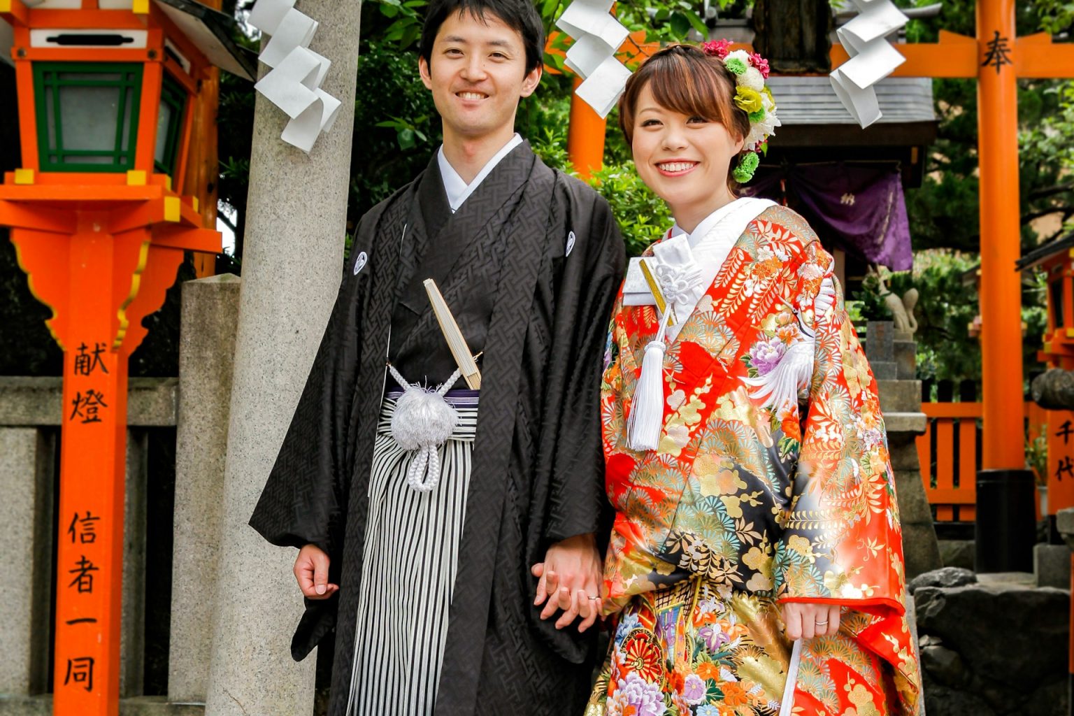 神社の鳥居の前に立つ、色打掛と紋付袴の二人