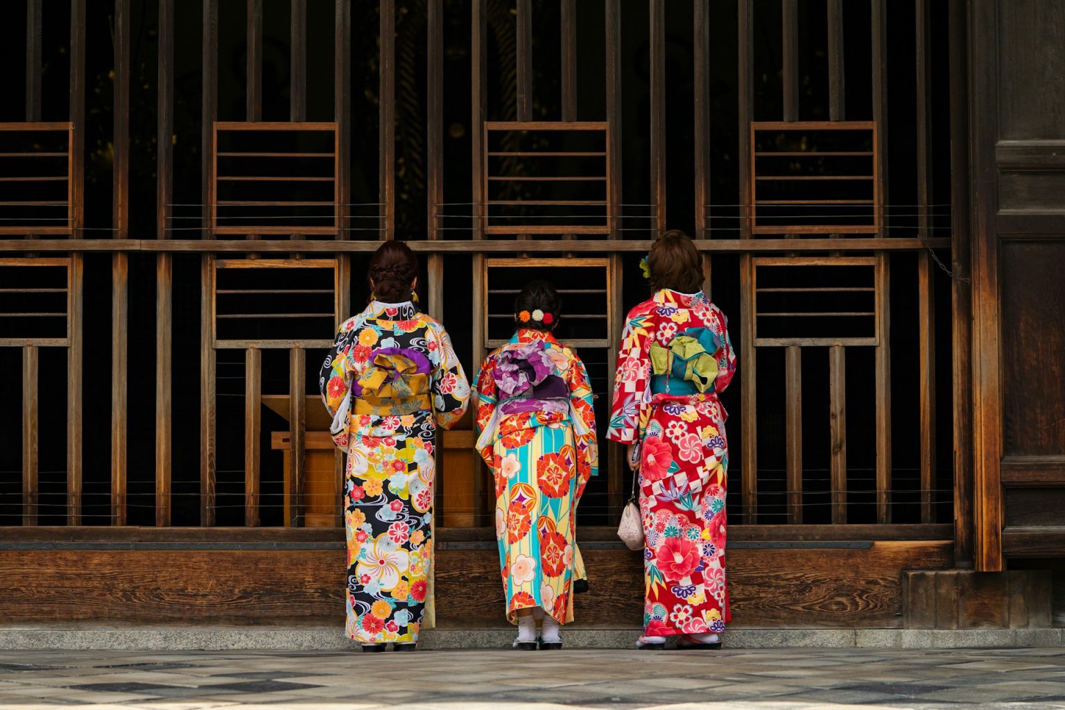 格子戸の前に並ぶ、色とりどりの着物姿の三人の後ろ姿